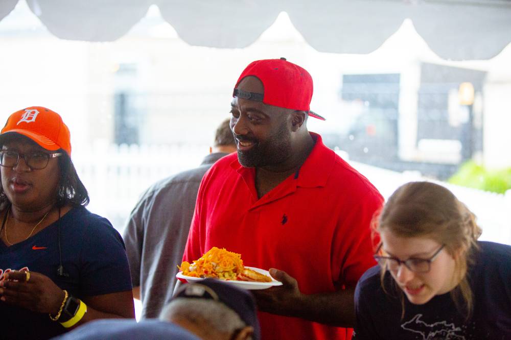 A smiling father waiting in the food line at the party. He has on a cool red snapback